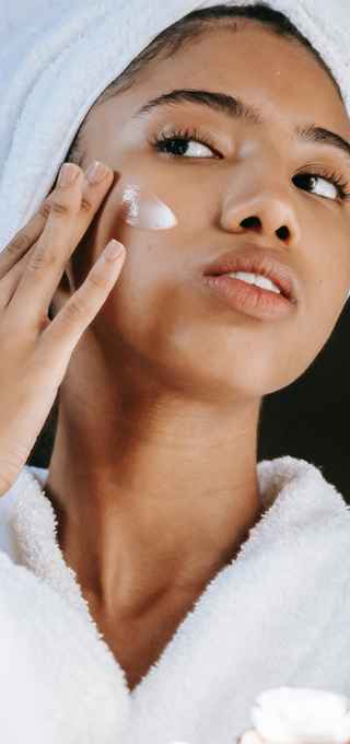 Woman looking at mirror while putting face cream on