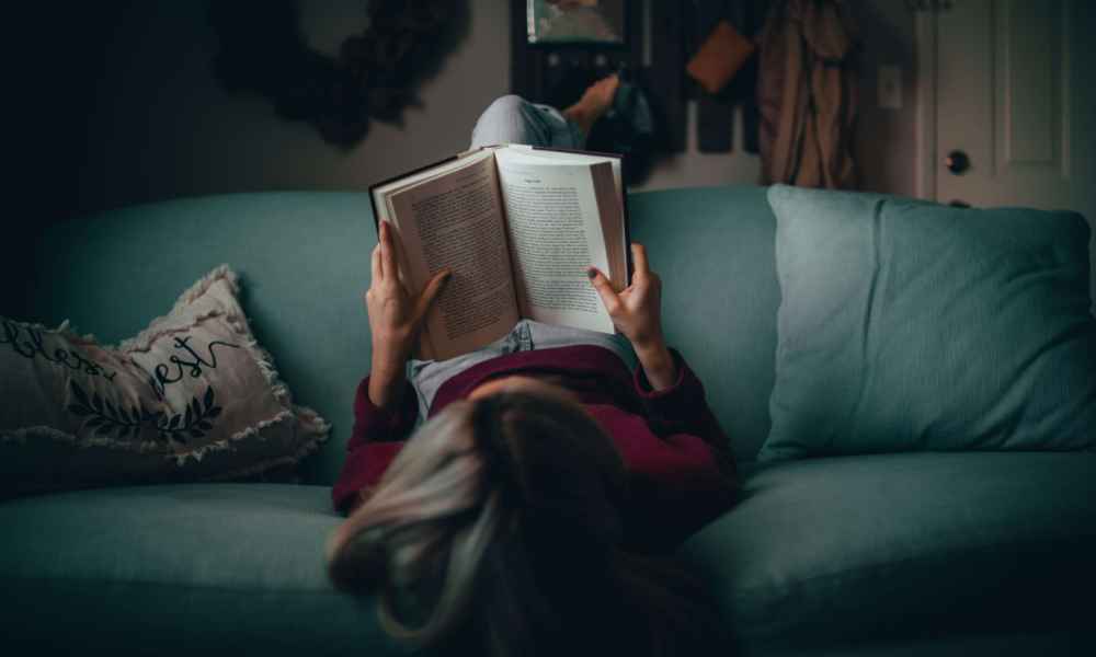 women laying on sofa reading a book