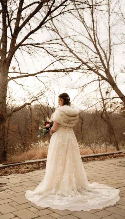 Woman in her bride dress and fur coat holding bouquet