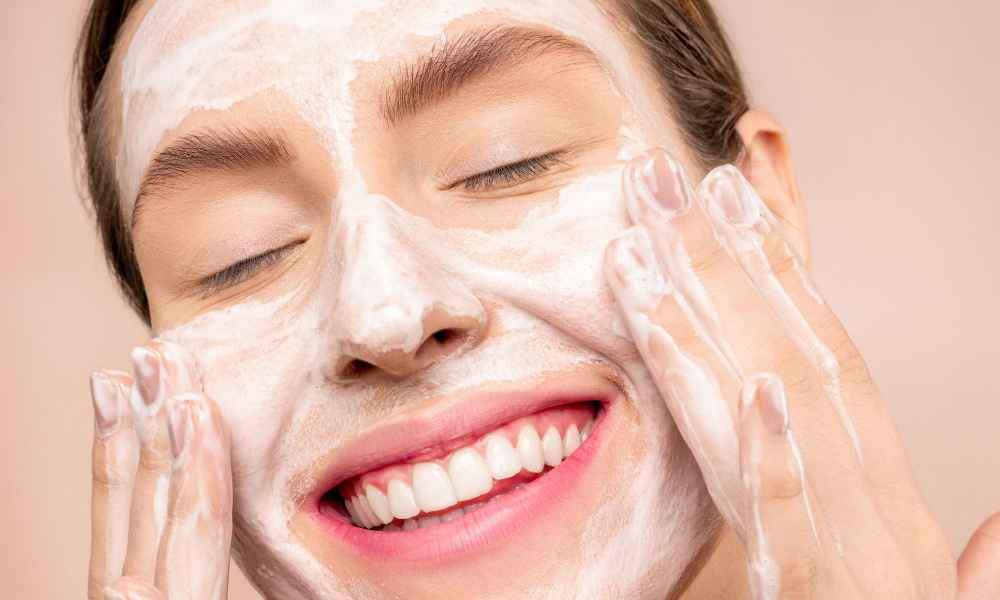 Woman smiling while cleansing her face 