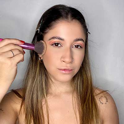 Girl applying bronzer on her face.