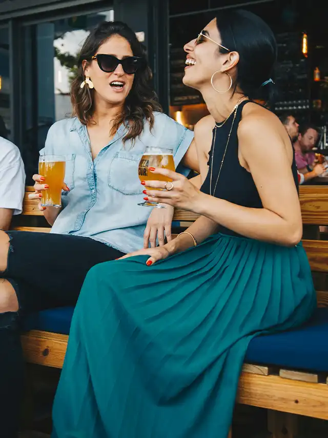 two women sitting on a bench holding drinks