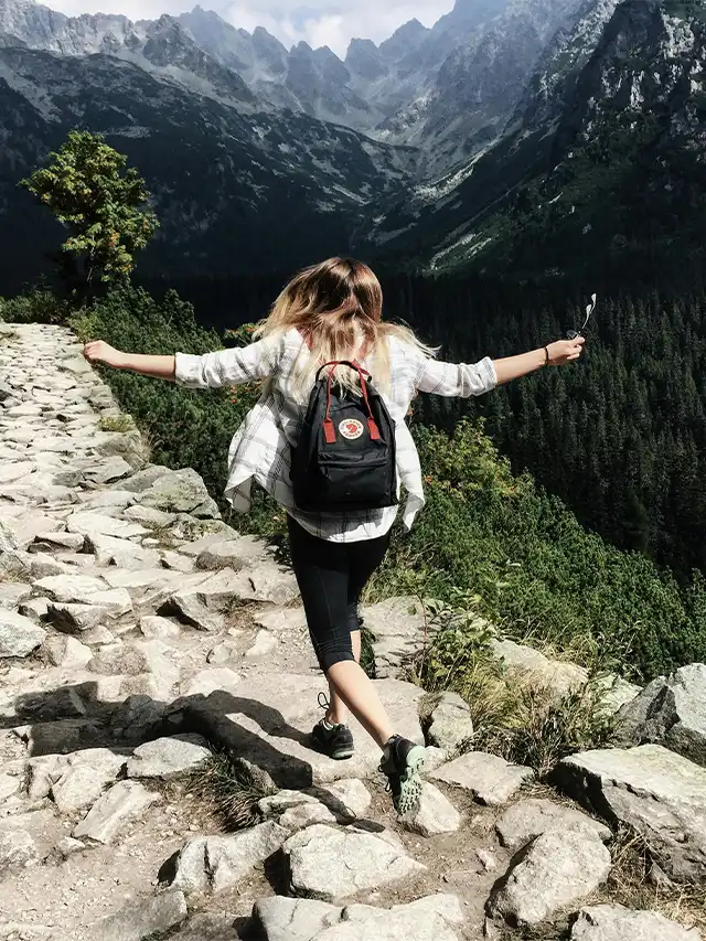 a woman walking on a rocky path with her arms outstretched