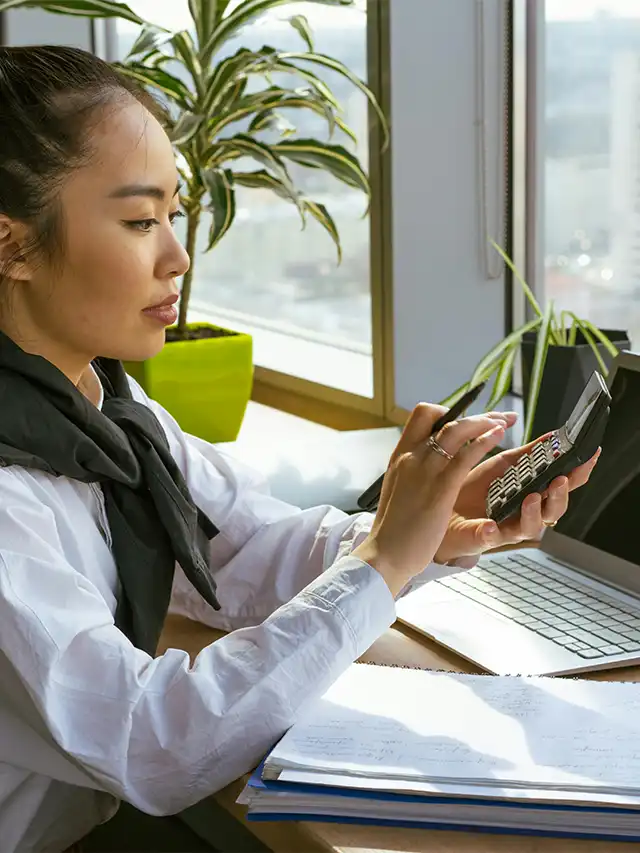 a woman holding a calculator and looking at a laptop