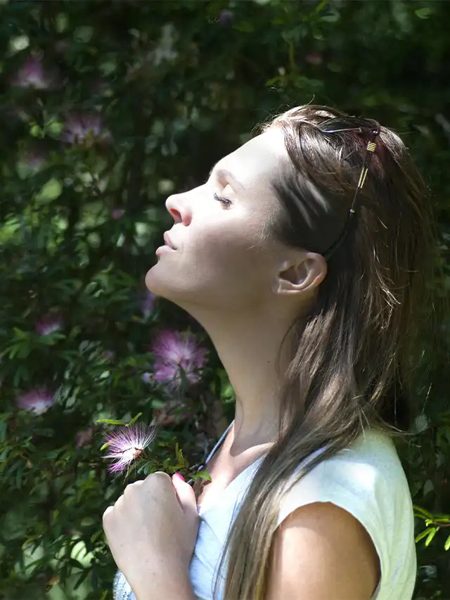 a woman with eyes closed standing in front of a bush