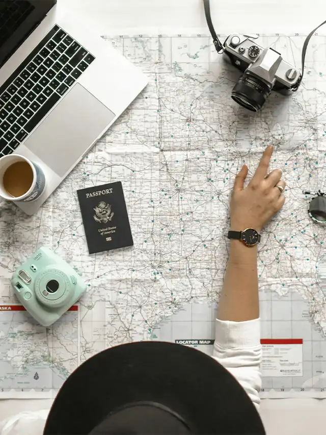 a hand pointing at a map with a laptop and a camera