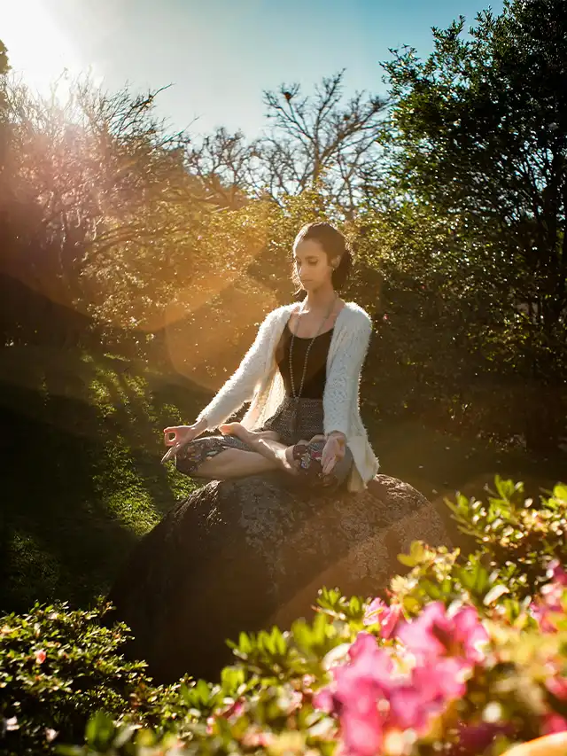 a woman sitting on a rock in the sun