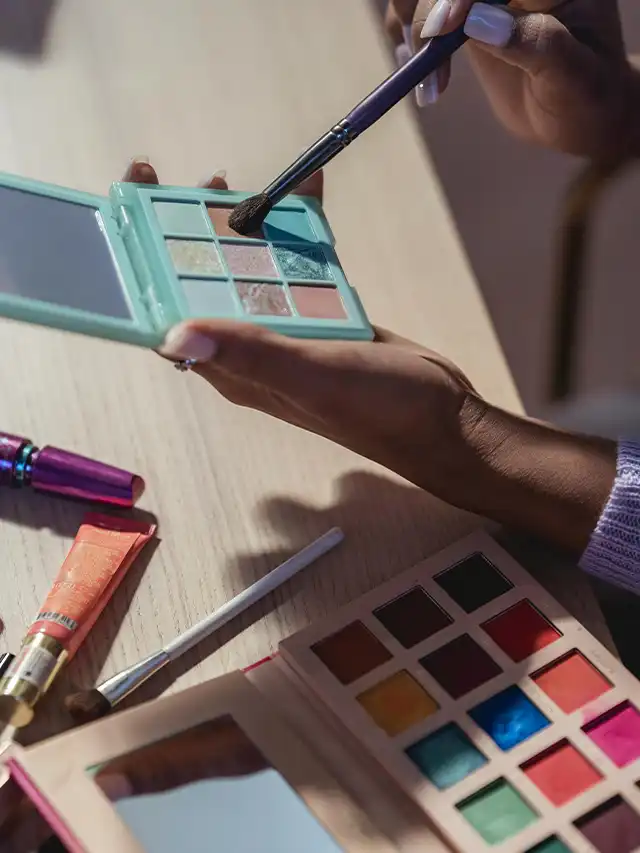 a hand holding a makeup brush and a small mirror