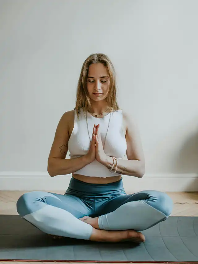 a woman sitting cross legged with hands together in front of her